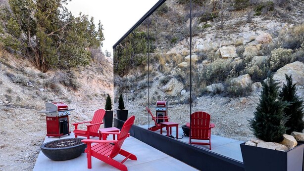 Une terrasse extérieure avec des fauteuils Adirondack rouges, un barbecue et un foyer.