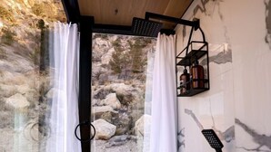 Une salle de bain moderne avec une douche, des rideaux blancs et une vue sur un paysage rocheux.