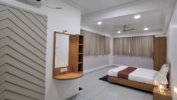 A modern bedroom with a bed, bedside table, and a built-in shelf with a mirror. - HOTEL HEAVEN  (Ahmedabad)