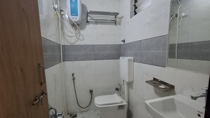 A small bathroom with a toilet, sink, and shower. There is a towel rack and a mirror on the wall. - HOTEL HEAVEN  (Ahmedabad)