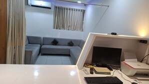 A modern living room with a grey sofa, a white desk with a computer, and a ceiling fan. - HOTEL HEAVEN  (Ahmedabad)