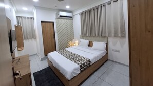 A modern bedroom with a wooden bed, a ceiling fan, an air conditioning unit, a wooden wardrobe, and a mirror. - HOTEL HEAVEN  (Ahmedabad)