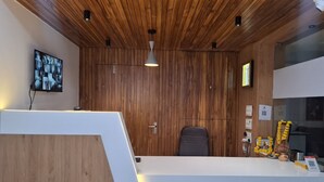 A reception area with a wooden ceiling, a flat-screen TV mounted on the wall, a white reception desk, a black office chair, and a small shrine with flowers. - HOTEL HEAVEN  (Ahmedabad)