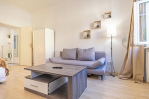 Ein modernes Wohnzimmer mit einer Couch, einem Couchtisch, einer Stehlampe und einem Fenster mit Vorhängen.