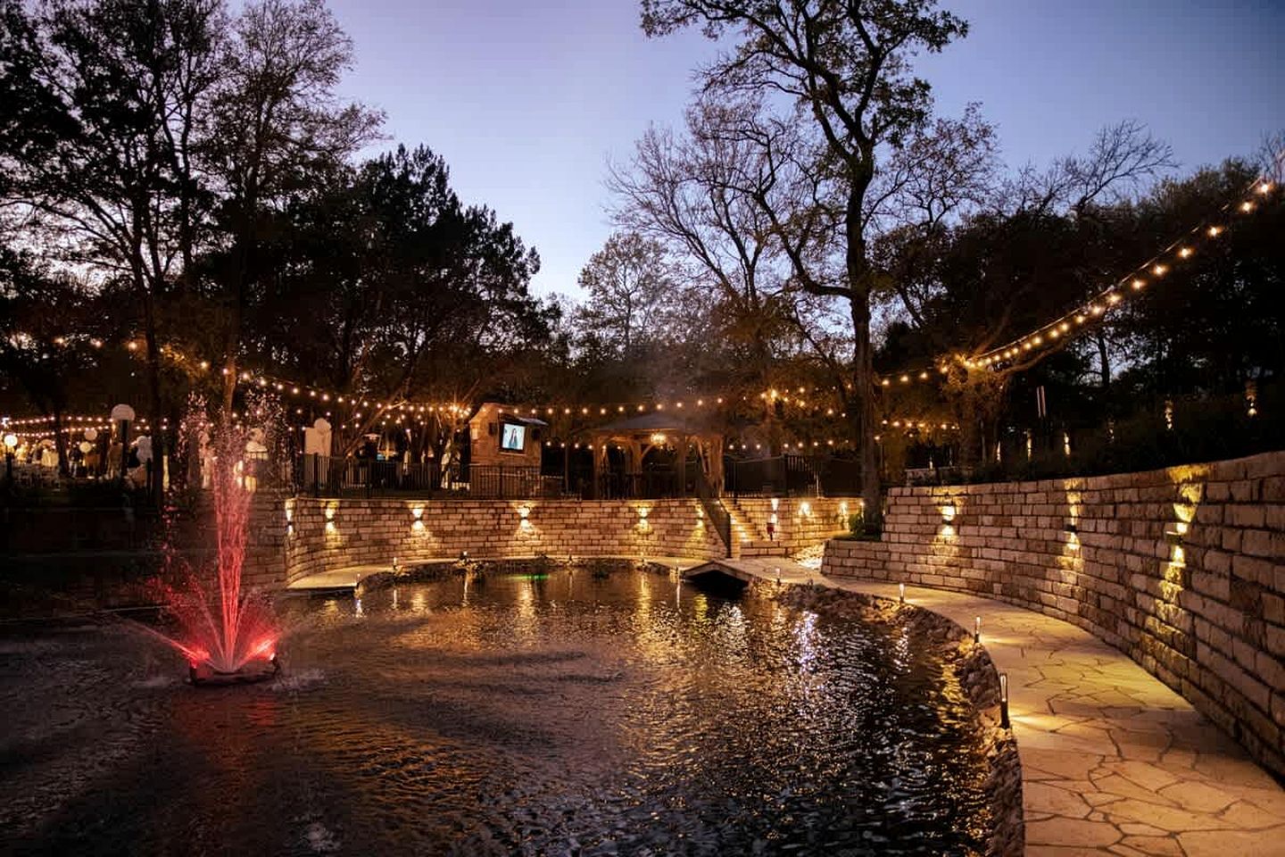 A courtyard with a water feature, stone walls, and string lights.