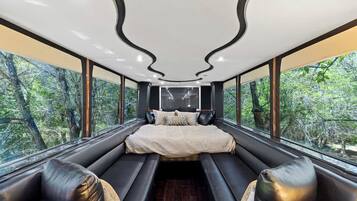 A modern bedroom with a large bed, seating area, and large windows offering a forest view.