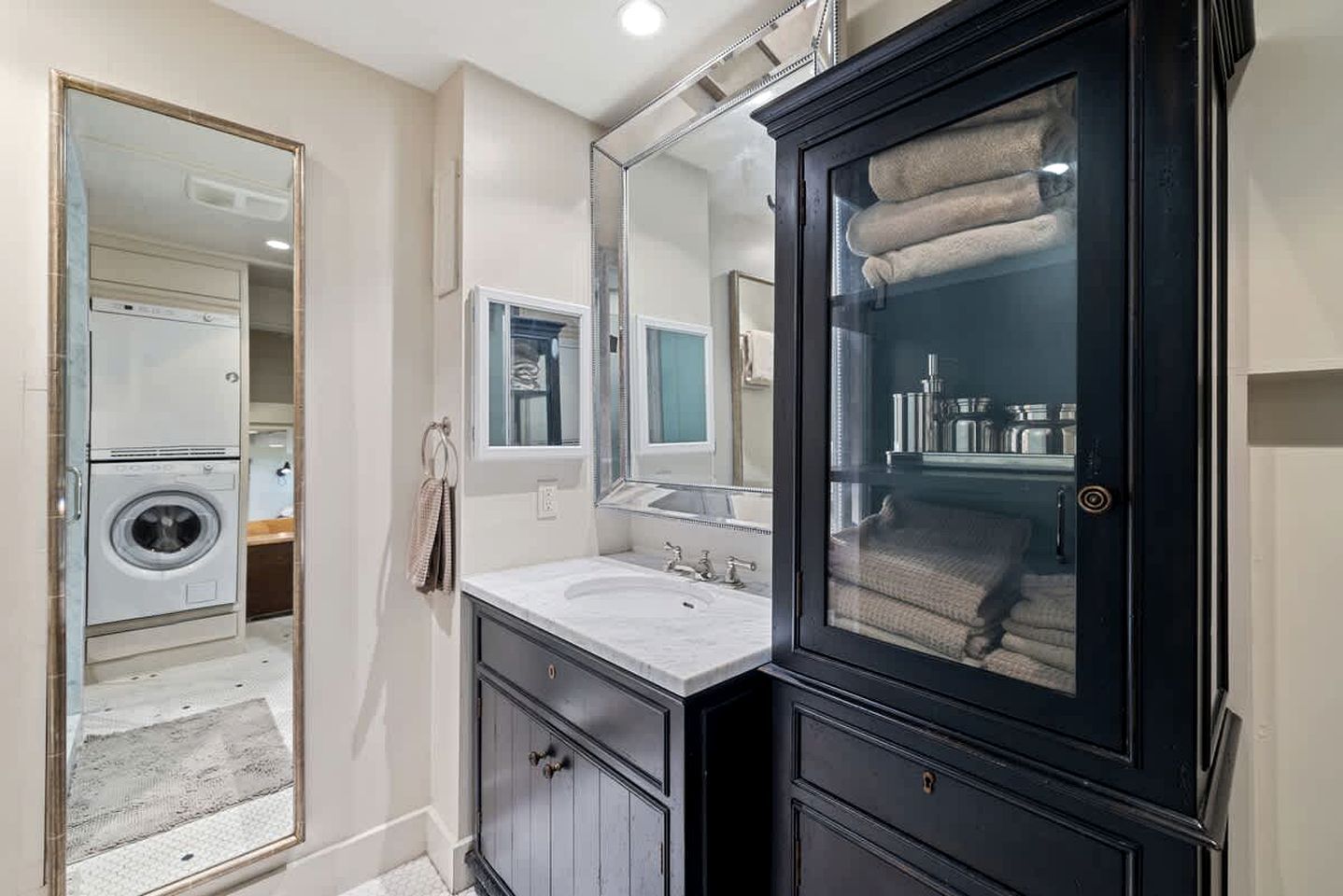 A bathroom with a large mirror, a sink, a cabinet, and a washing machine.