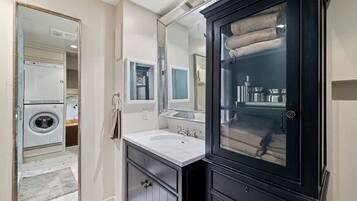 A bathroom with a large mirror, a sink, a cabinet, and a washing machine.