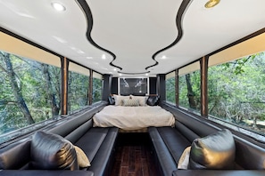 Un intérieur moderne comprenant un lit, un coin salon et de grandes fenêtres donnant sur la forêt.