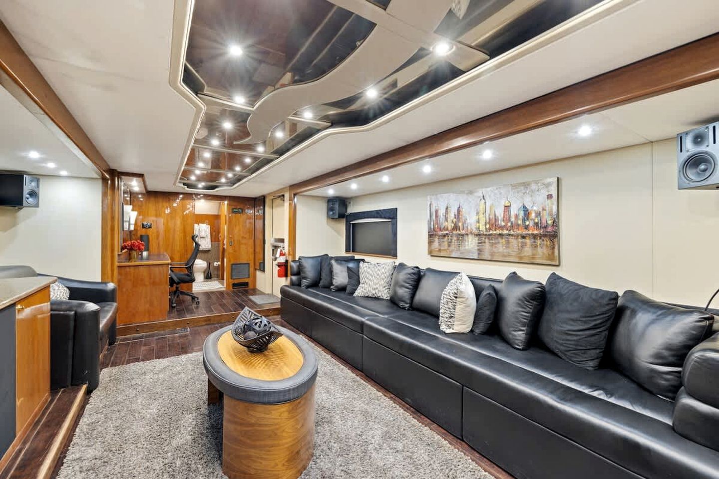 A modern living room with a black leather sofa, a wooden coffee table, and a cityscape painting on the wall.