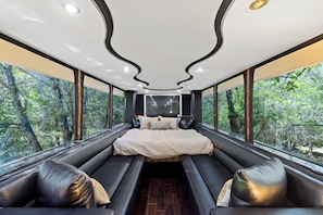 Un dormitorio moderno con una cama grande, zona de estar y ventanas amplias con vistas a un bosque.