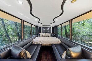 Quarto moderno com cama grande, área de estar e amplas janelas com vista para a floresta.