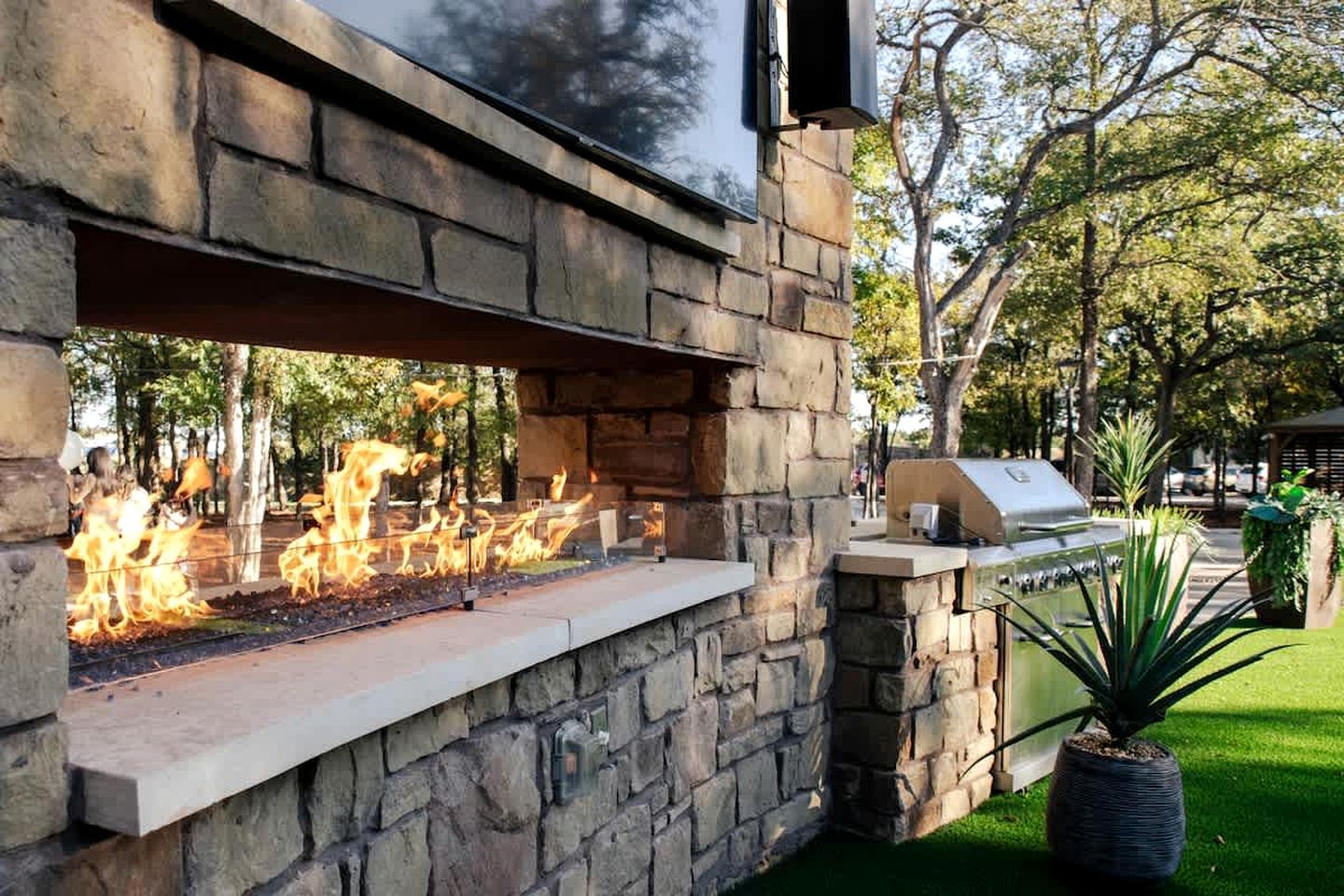 An outdoor stone wall with a built-in fire feature and a grill.