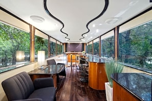 Un interior moderno con una larga mesa, sillas, zona de bar y ventanas amplias que ofrecen vistas al exterior.