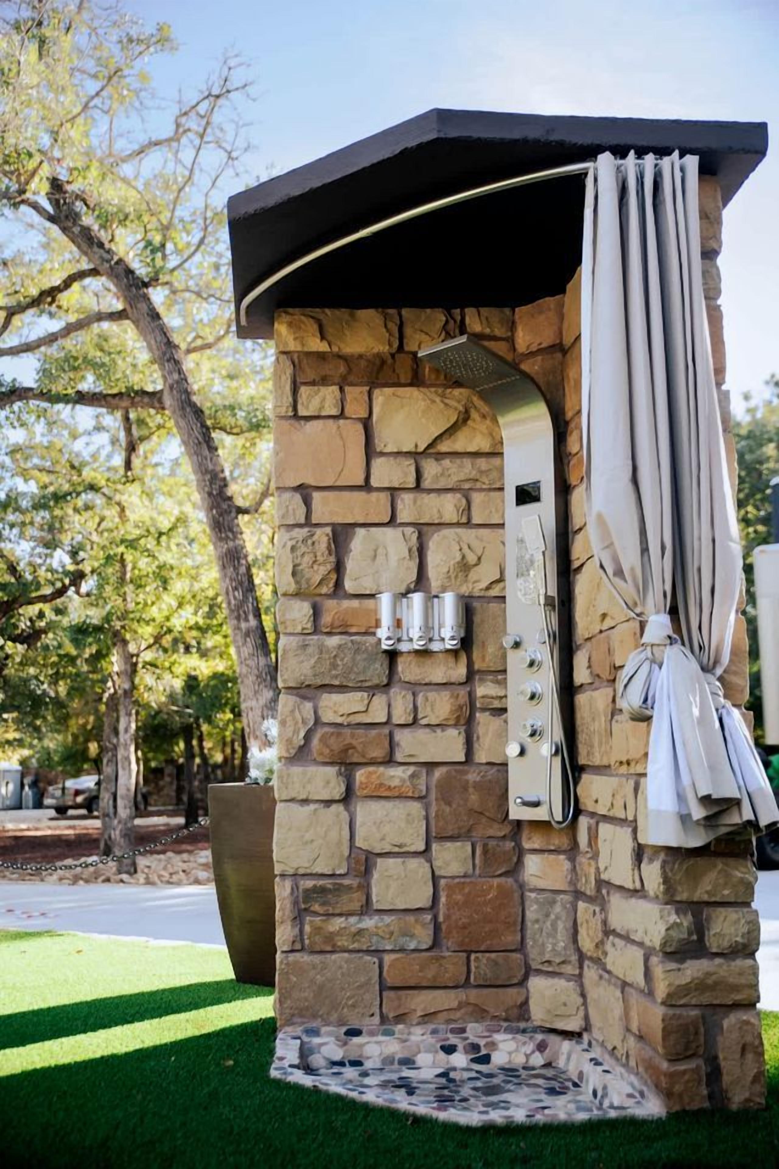 An outdoor grill structure with stone walls, a metal hood, and a hanging umbrella.