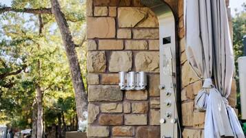 An outdoor grill structure with stone walls, a metal hood, and a hanging umbrella.