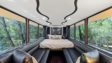 A modern bedroom with a large bed, seating area, and large windows offering a forest view.