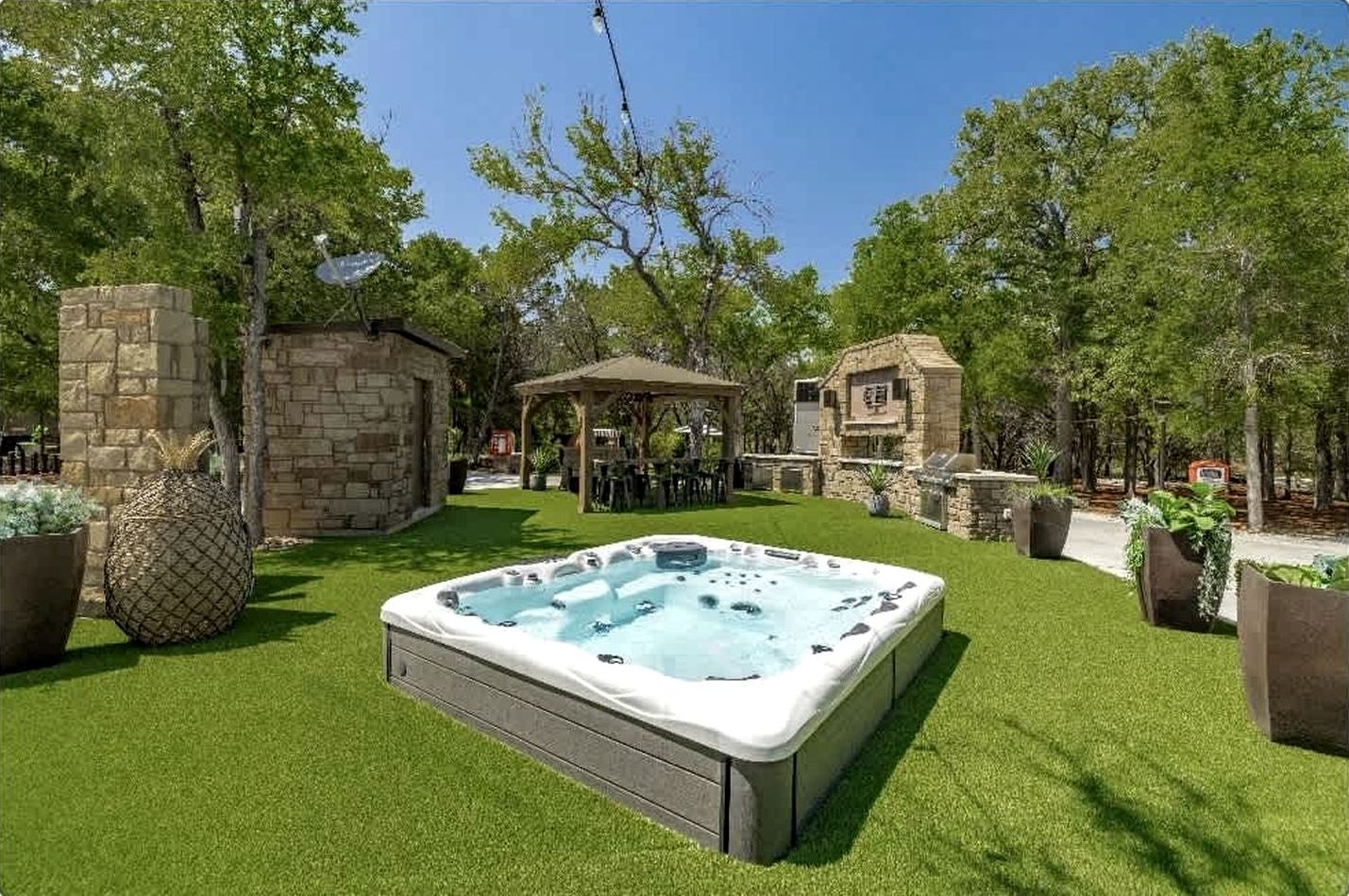 A hot tub in a backyard with stone walls, a pergola, and potted plants.