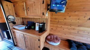 Ein Holzblockhaus-Innenraum mit Küchenzeile, einem an der Wand befestigten Fernseher und einer gemütlichen Sitzecke mit Kissen.