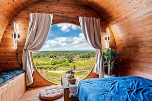 A circular wooden room with a bed, a small table, and a view of a vineyard.