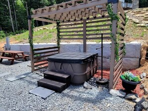 Et spabad under en træpergola med trin op til det, omgivet af grus og krukkeplanter.