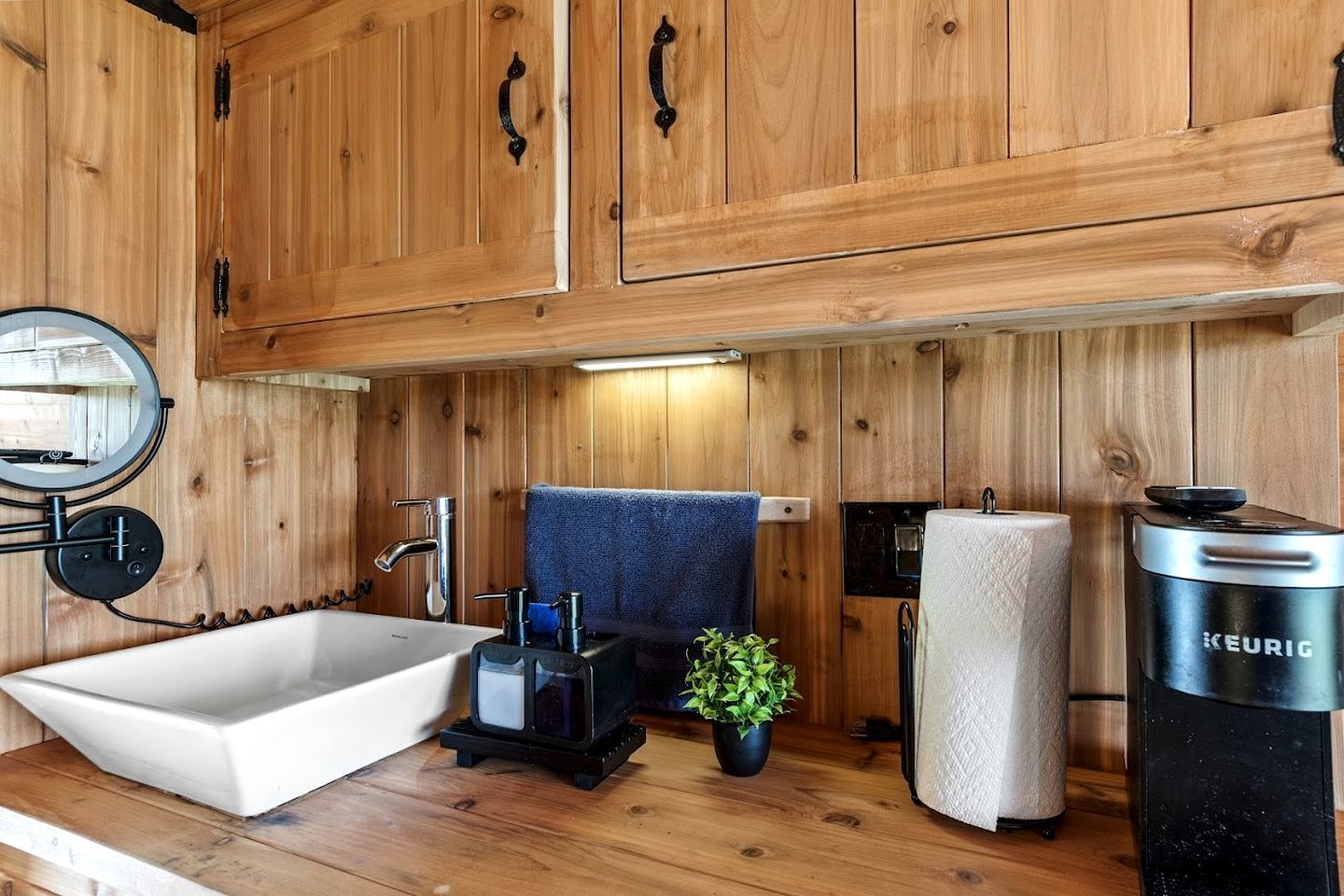 A wooden cabin interior with a white bathtub, a sink, a mirror, a towel, a plant, and a Keurig coffee maker.