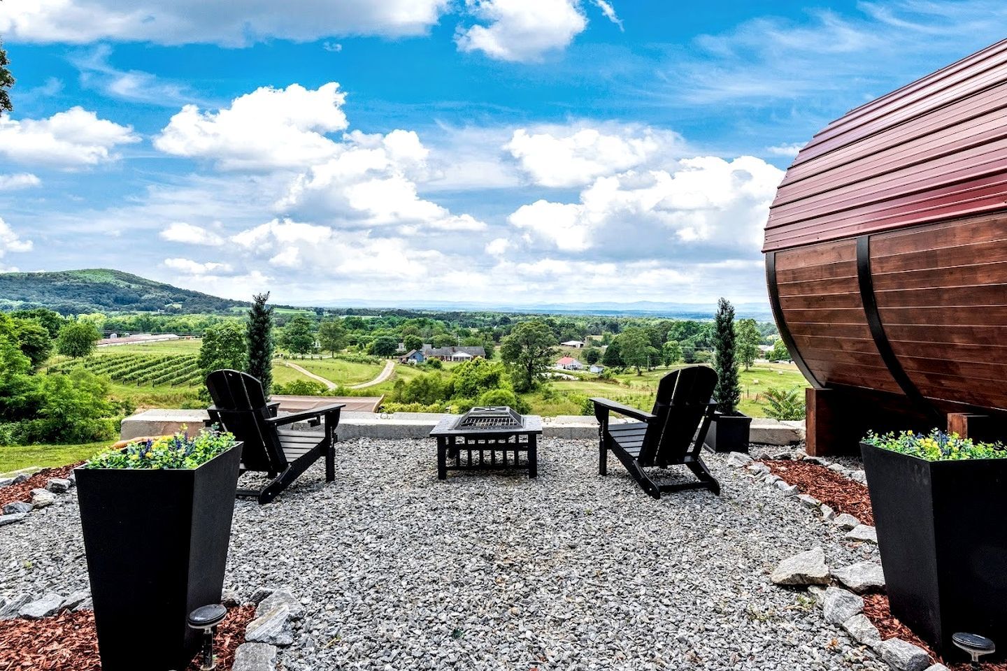 A patio with two Adirondack chairs, a table, and a large wooden barrel.
