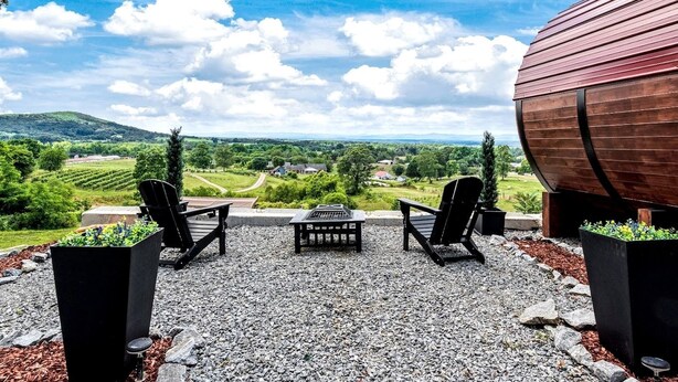 Eine Terrasse mit zwei Adirondack-Stühlen, einem Tisch und einem großen Holzfass.