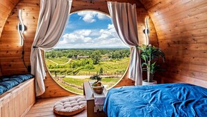 Ein kreisrunder Holzraum mit einem Bett, einem kleinen Tisch und Blick auf einen Weinberg.