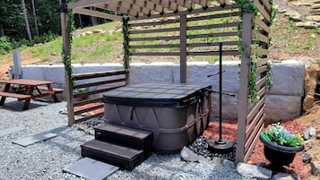 A hot tub under a wooden pergola with steps leading up to it, surrounded by gravel and potted plants.