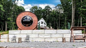 A wooden structure with a circular window, a white house, and a stone wall with chairs.