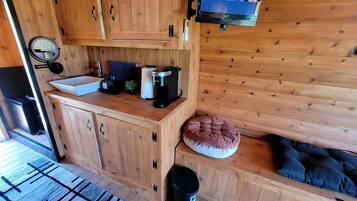 A wooden cabin interior with a kitchen area, a mounted TV, and a cozy seating area with cushions.