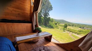 Ein Holzinnenraum mit einem Bett, einer Bank und einer gepolsterten Sitzecke. Ein Fenster bietet Blick auf eine grüne Landschaft.