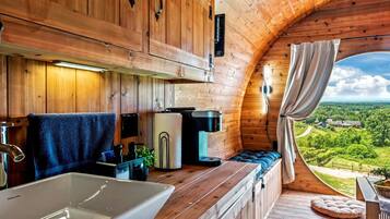 Une cabane chaleureuse avec un intérieur en bois, une grande fenêtre, un évier et un coin salon confortable.