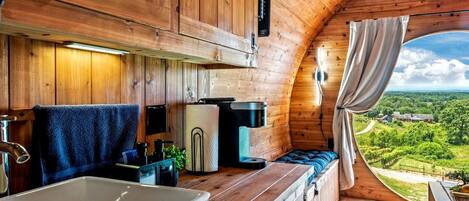 A cozy cabin with a wooden interior, a large window, a sink, and a cozy seating area.