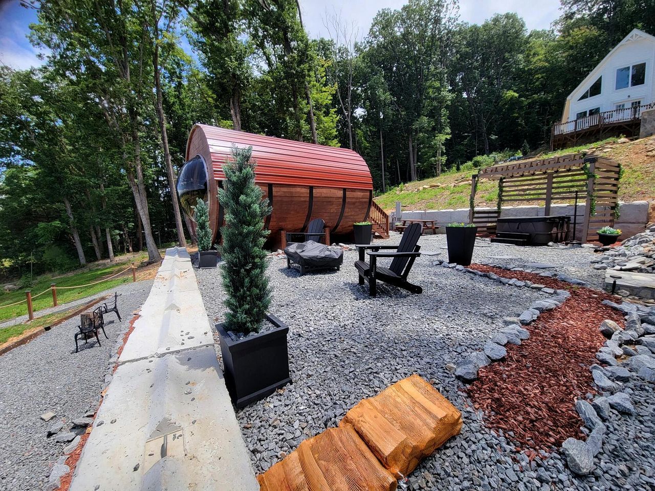 A covered outdoor seating area with a table and chairs, surrounded by a gravel path and a wooden deck.