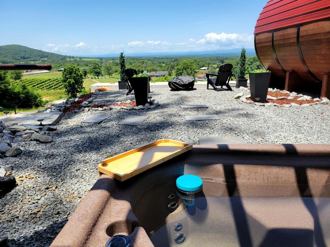 A rustic outdoor seating area with a view of vineyards, a large barrel, and a wooden tray.