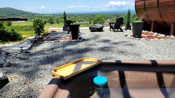 A rustic outdoor seating area with a view of vineyards, a large barrel, and a wooden tray.