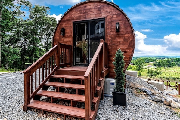 Eine Holzhütte mit einer Treppe, die zu einer Tür führt, umgeben von Kies und Grünpflanzen.