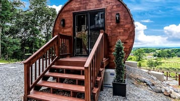 Une cabane en bois avec un escalier menant à une porte, entourée de gravier et de verdure.