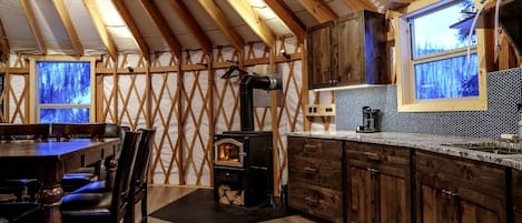 A rustic kitchen with a wood stove, wooden cabinets, and a dining area with a table and chairs.
