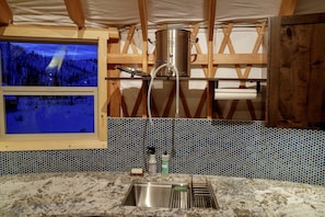 A kitchen with a large window, a stainless steel pot, and a sink.