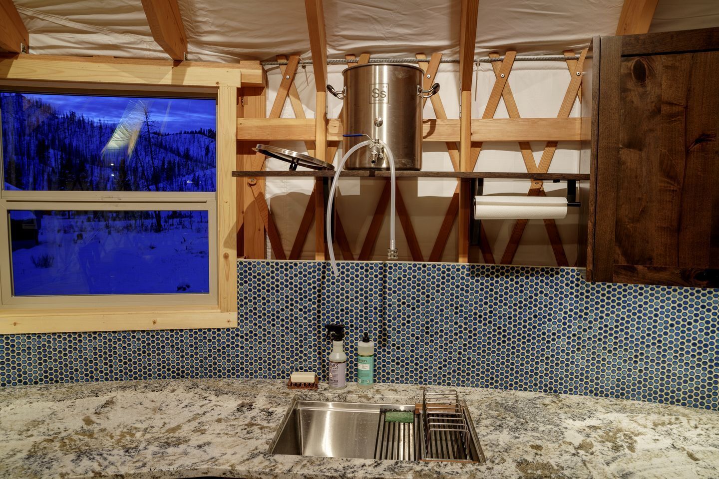 A kitchen with a large window, a stainless steel pot, and a sink.