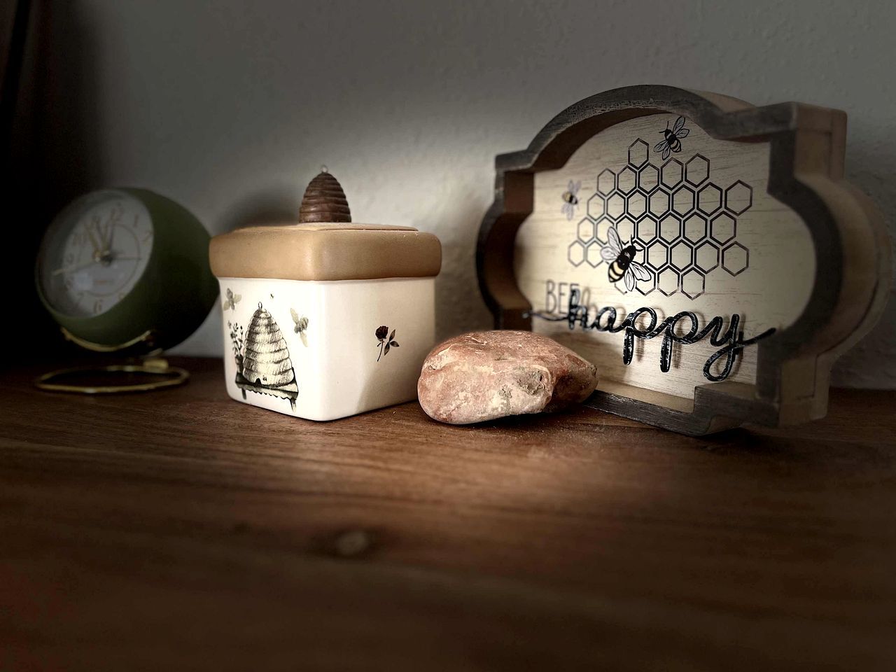 Een houten plank met een honingraatpatroon, een keramieken pot met deksel, een steen en een antieke klok.