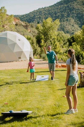 A grassy outdoor area with a white dome structure, a person walking, and a dog. - Family Friendly Cabin with BBQ in Glendale, Utah (Glendale)