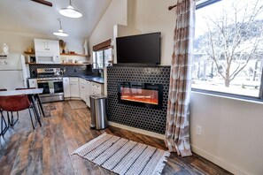 A modern kitchen with a fireplace, wooden flooring, and a dining area with a table and chairs. - Family Friendly Cabin with BBQ in Glendale, Utah (Glendale)