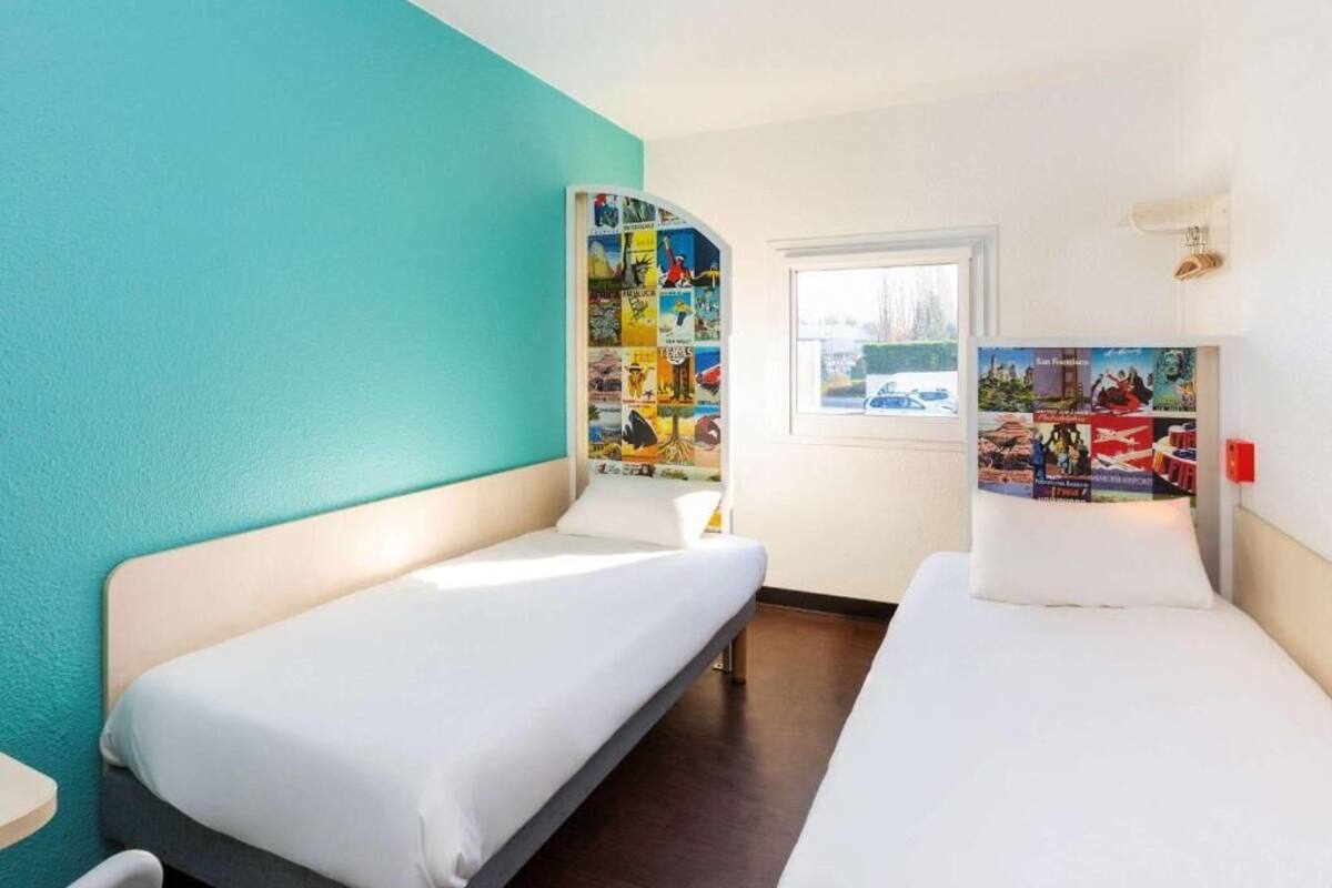 Habitación de hotel con dos camas individuales, ventana con vistas y pared decorada con carteles de viajes.