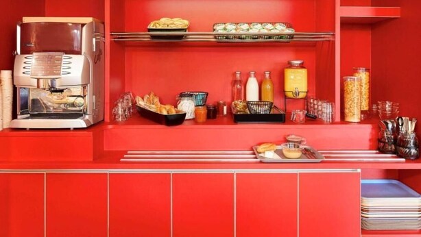 Zona de buffet color rojo con una cafetera, bandejas de comida y diversos condimentos.
