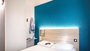 Una habitación de hotel con una cama, un estante con una chaqueta y una pared de acento azul.