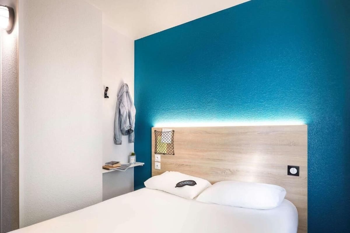 Una habitación de hotel con una cama, un estante con una chaqueta y una pared de acento azul.